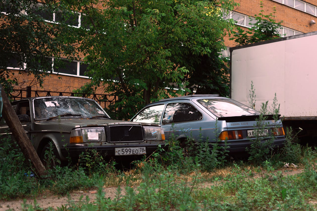 Abandoned vintage cars near a brick building in an urban environment.
